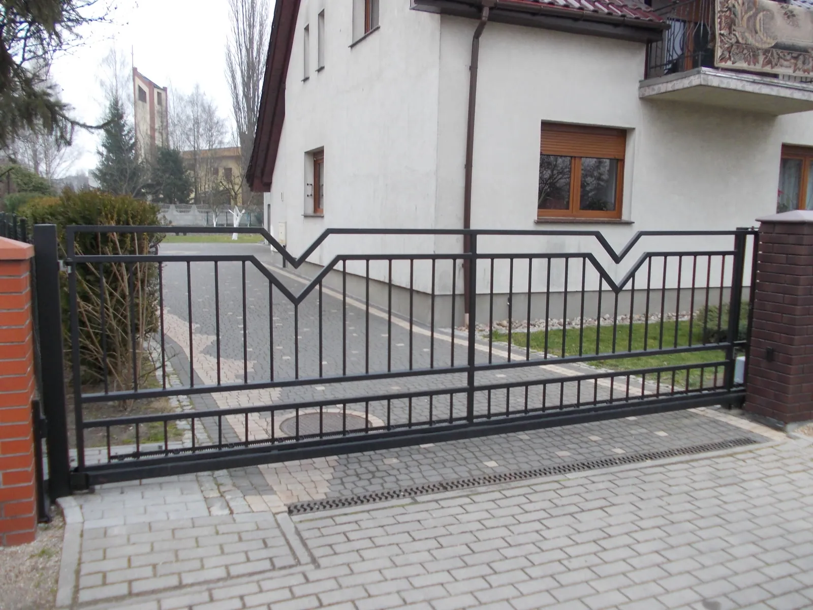 Brama przesuwna z ozdobnym wzorem V na szczycie przy domu