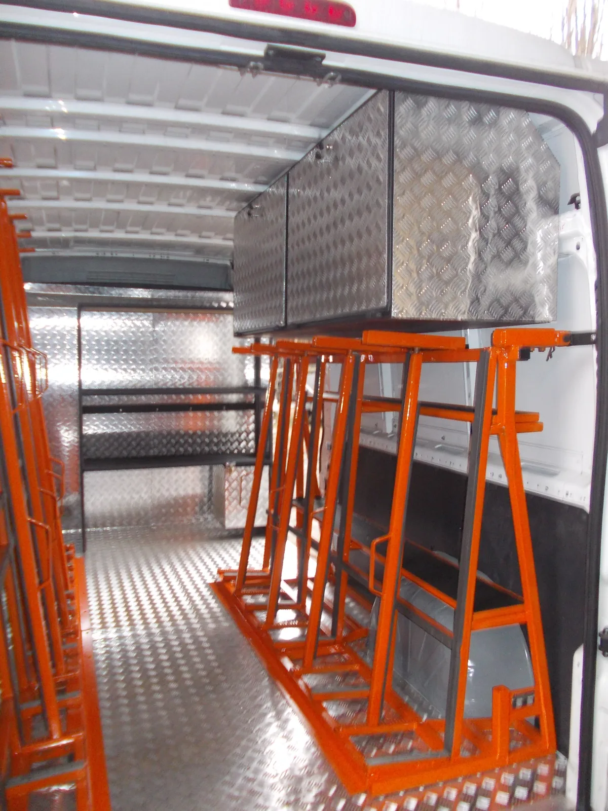 Pomarańczowe stojaki transportowe i aluminiowe szafki podsufitowe w zabudowie busa