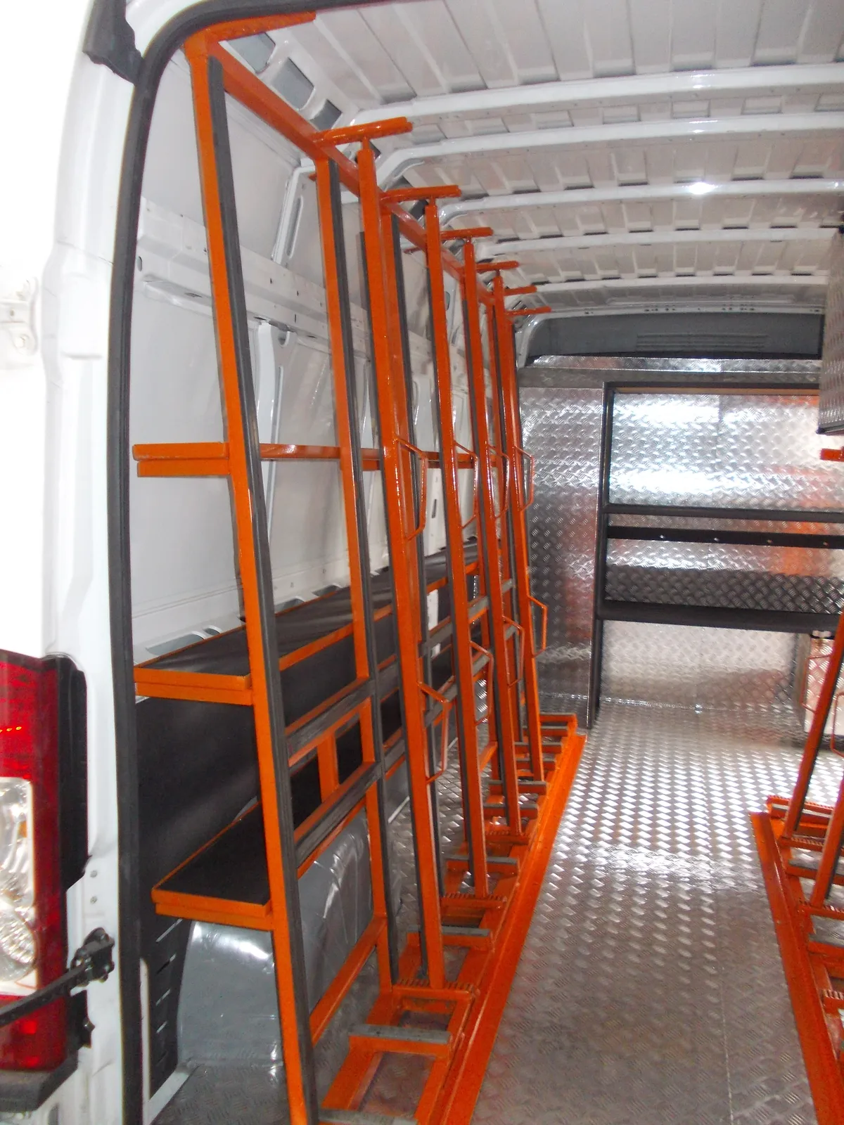 Rząd pomarańczowych stojaków transportowych wzdłuż ściany busa wyłożonego blachą ryflowaną